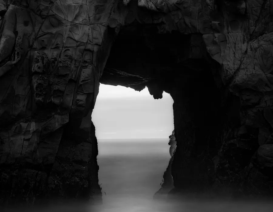 Sunlight streaming through the mouth of a coastal sea cave onto the ocean